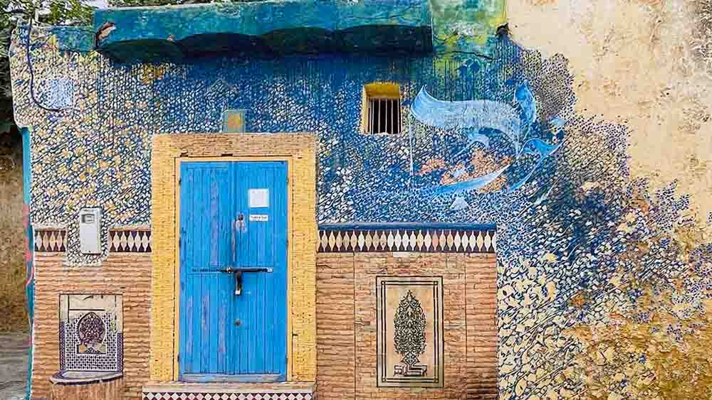 Whimsical street art in blue and gold colors on the outside of rustic art gallery in Asilah, Morocco.