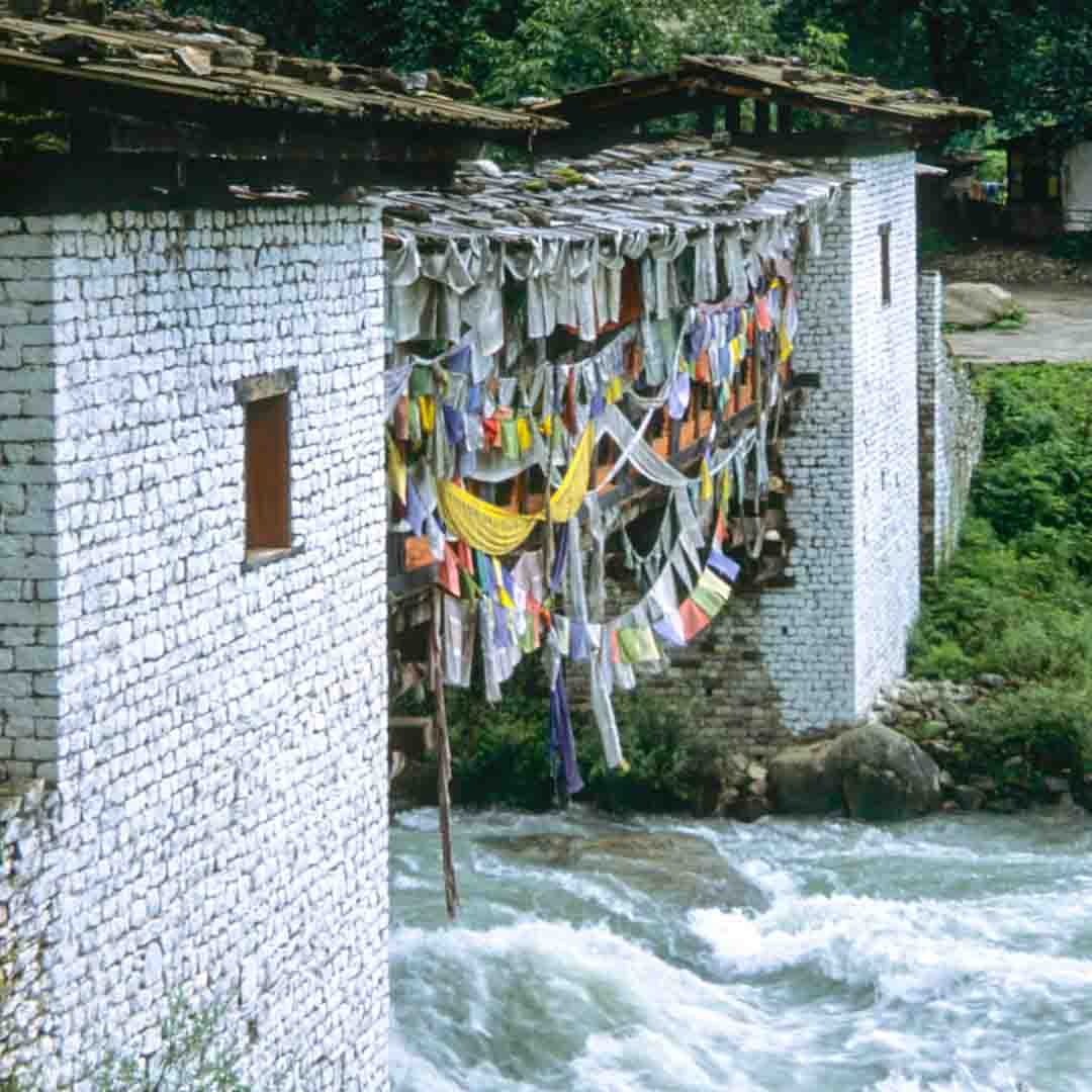 Prayer flags hanging from a bridge over a river.