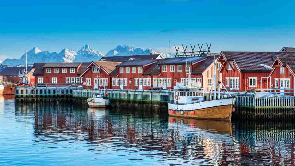 Red fisherman's huts in Svolvaer port with sailboat on the water.